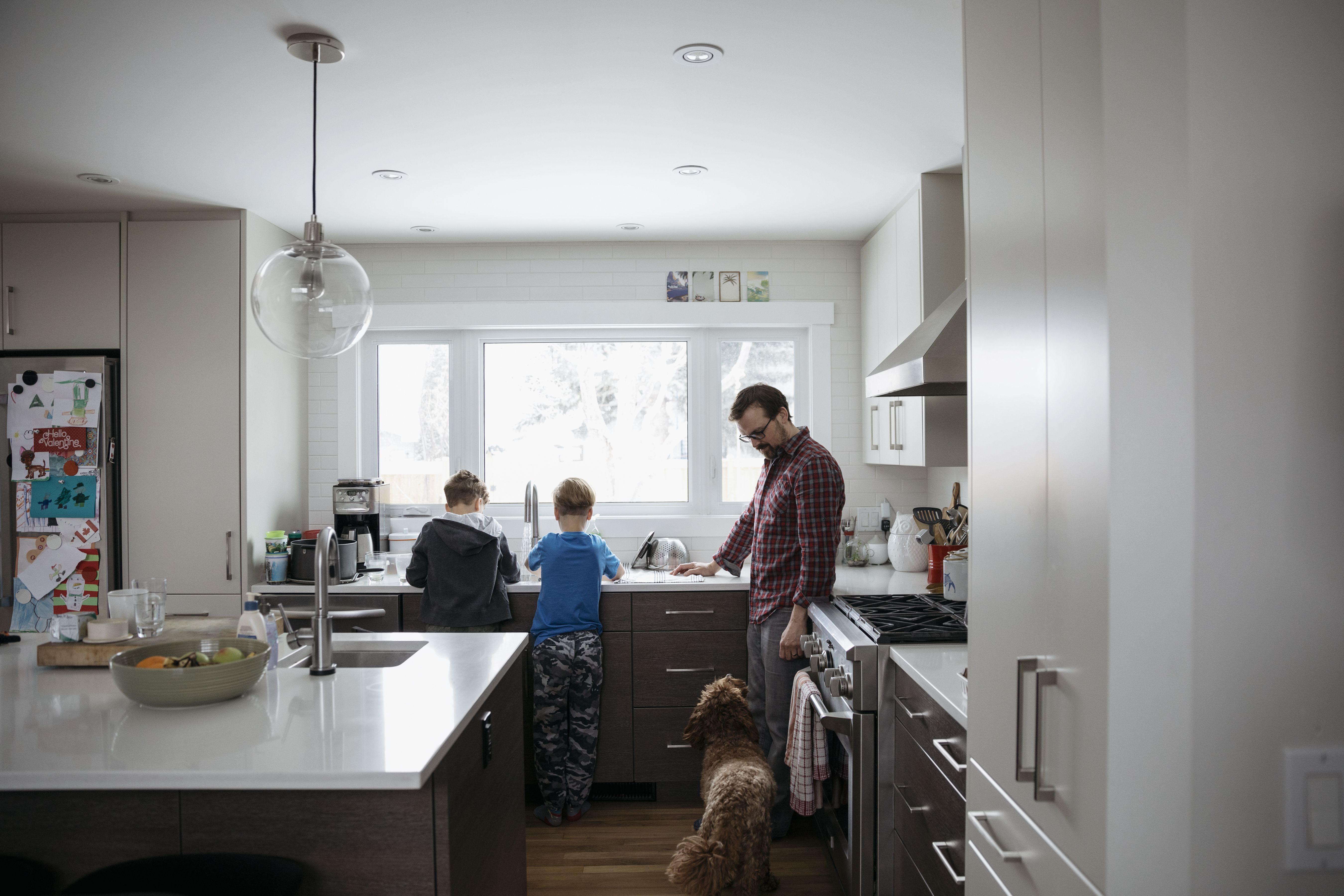 Dog watching father and sons doing dishes at kitchen sink