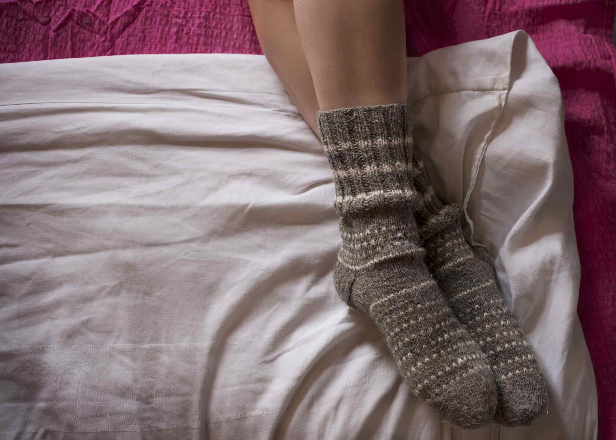 Woman wearing warm gray socks while lying on a bed.