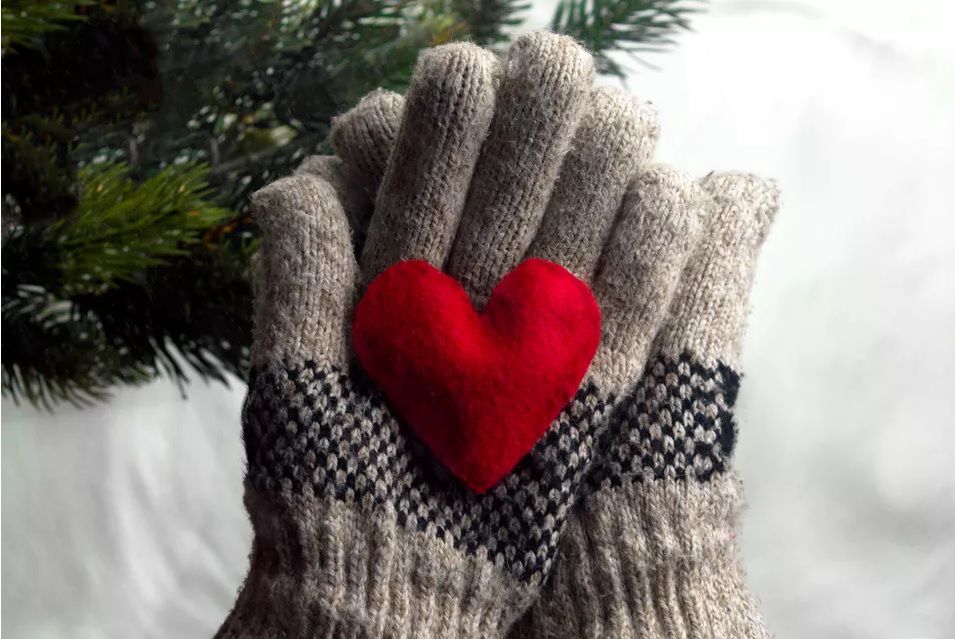 Two gray gloves holding a felt red heart.