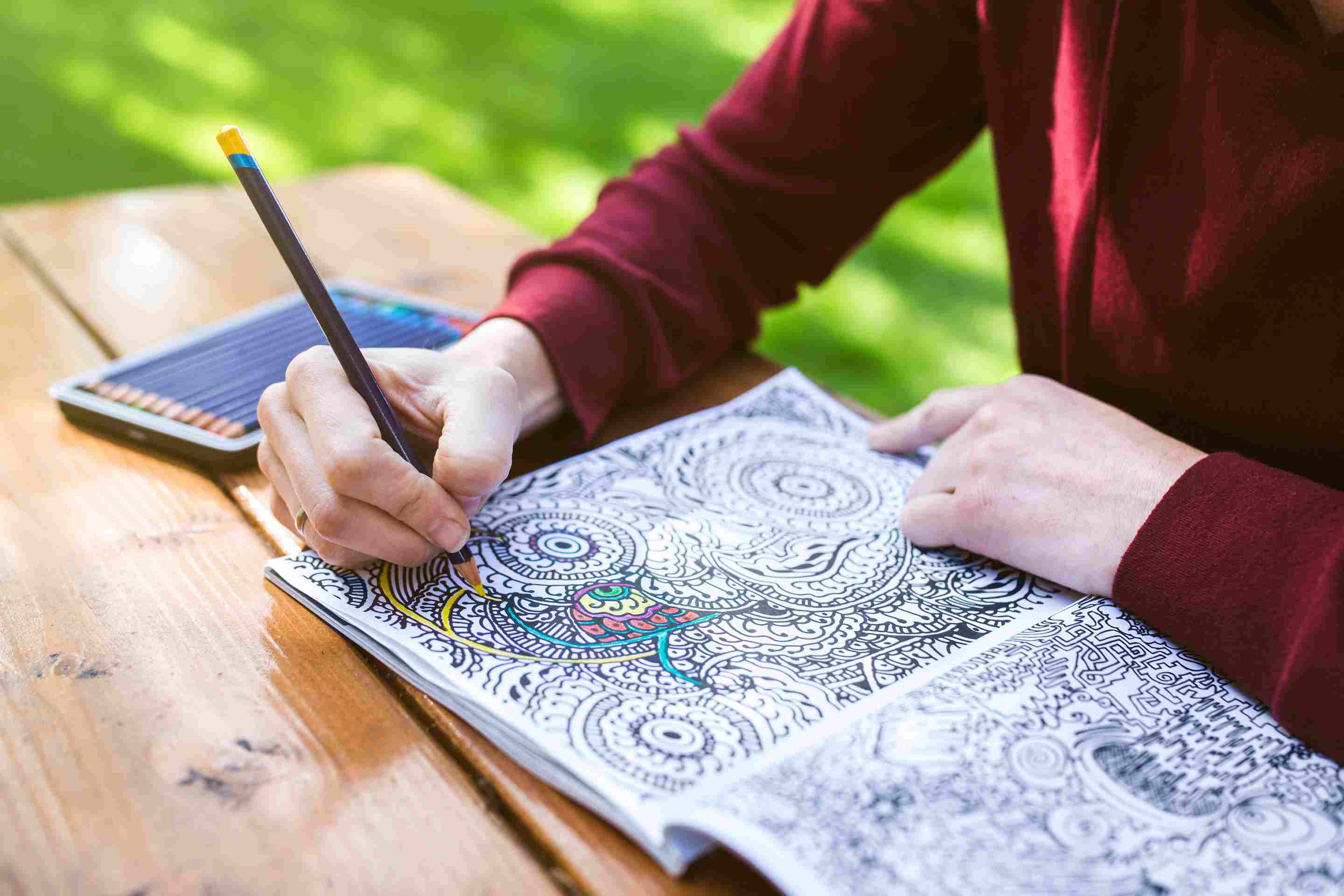 Woman using a coloring pencil to color an intricate coloring book.