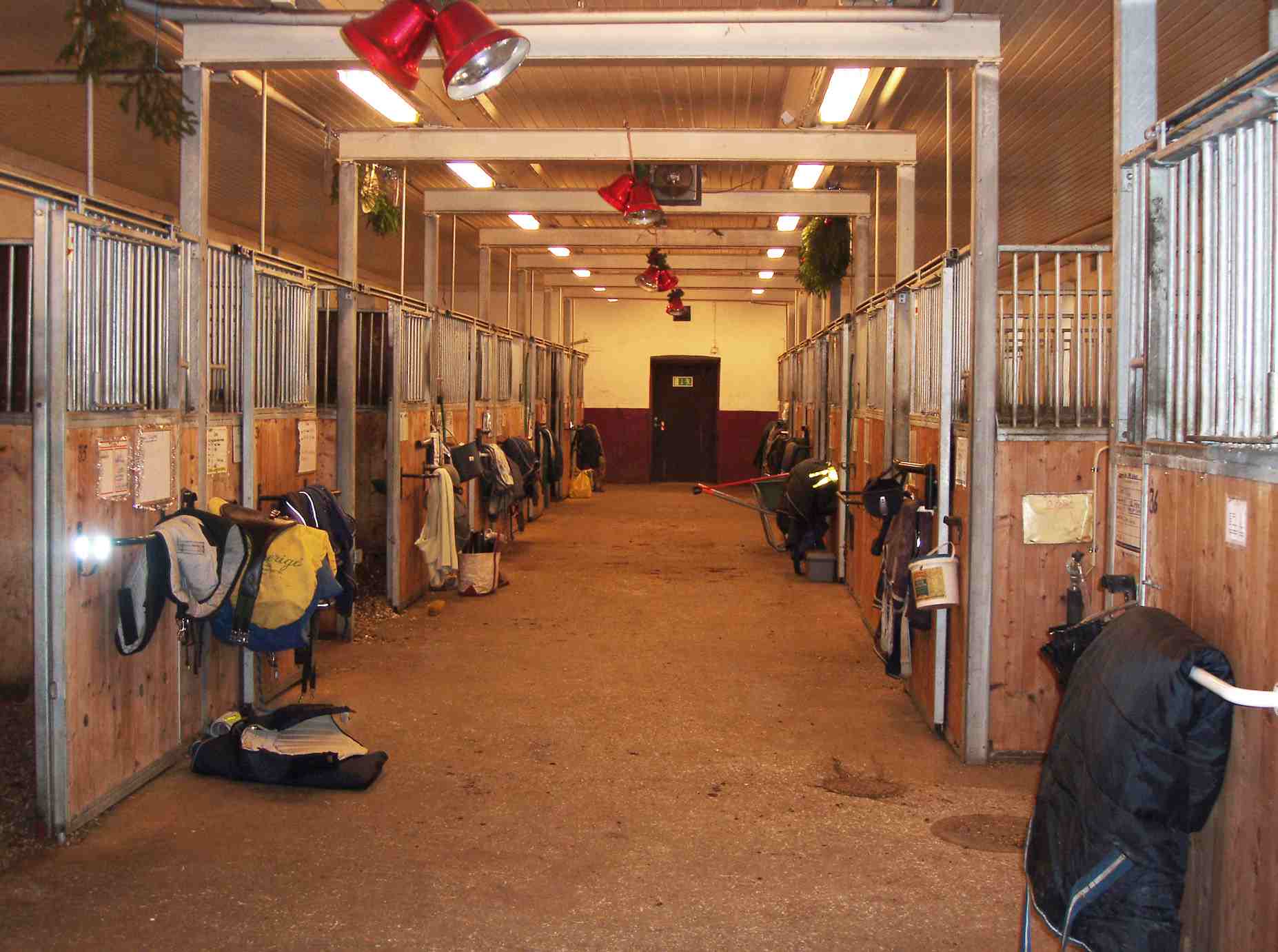 Inside of a stable showing aisle and tack outside of stalls.