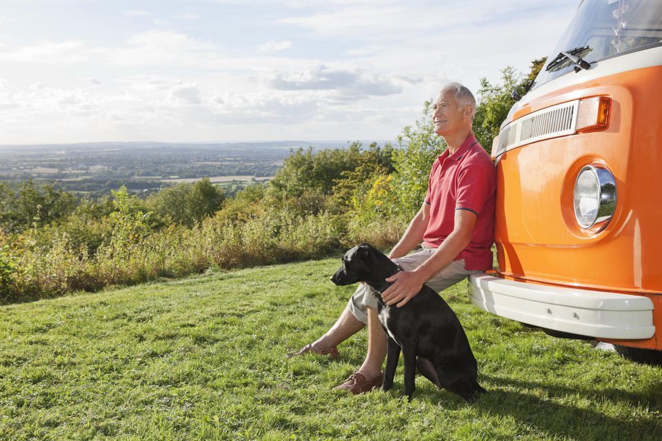 Senior man sitting on a bumper of a camper van with his dog.