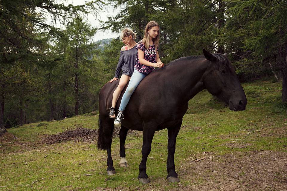 Girl and woman sitting bareback on horse in a forest.