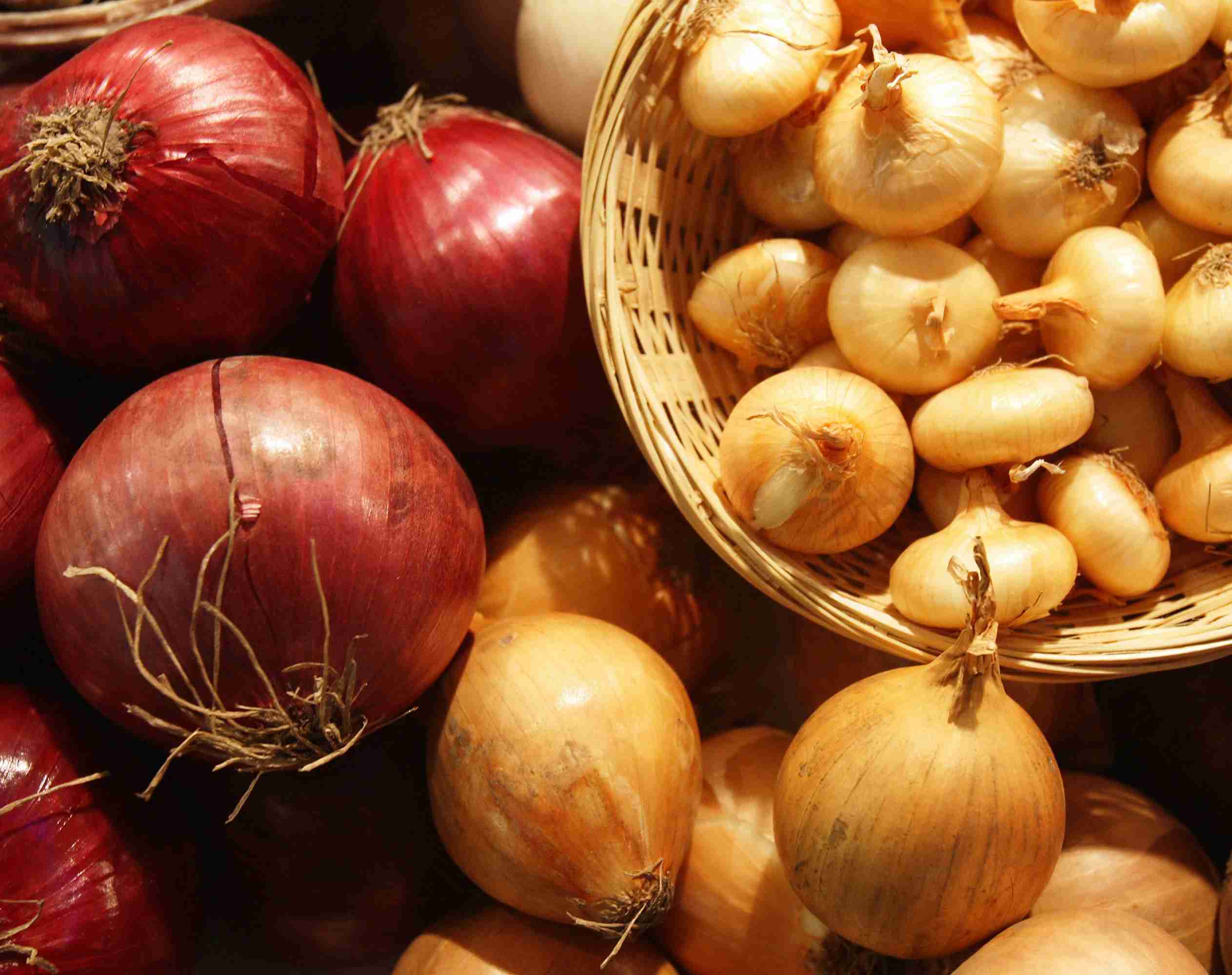 A variety of red and yellow onions, with the yellow ones in a basket.