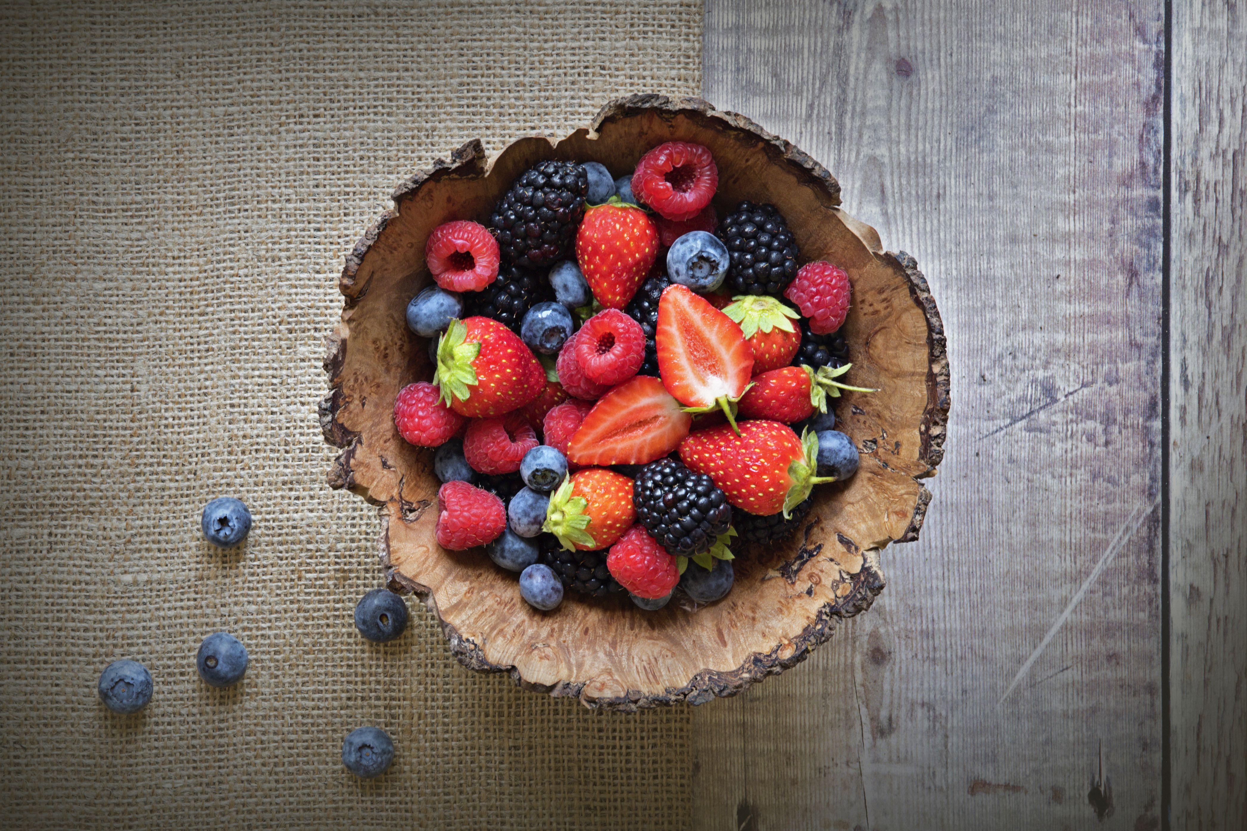 Close-up image of a wooden bowl full of berries including strawberries, raspberries, black berries, and blue berries.