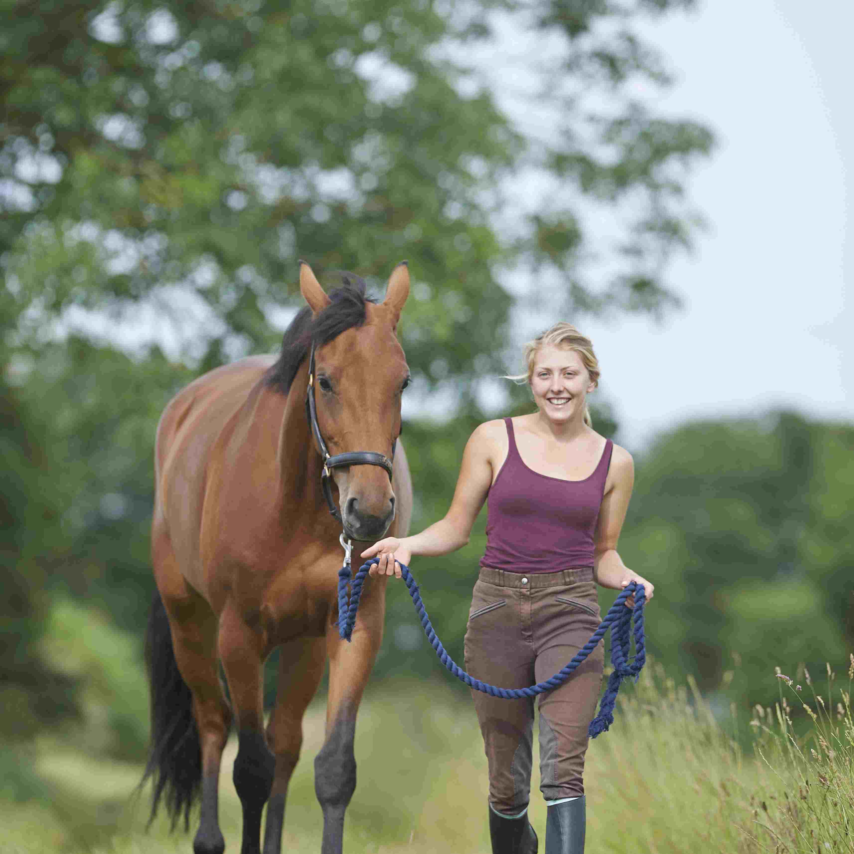 Young woman walking with horse in countryside.